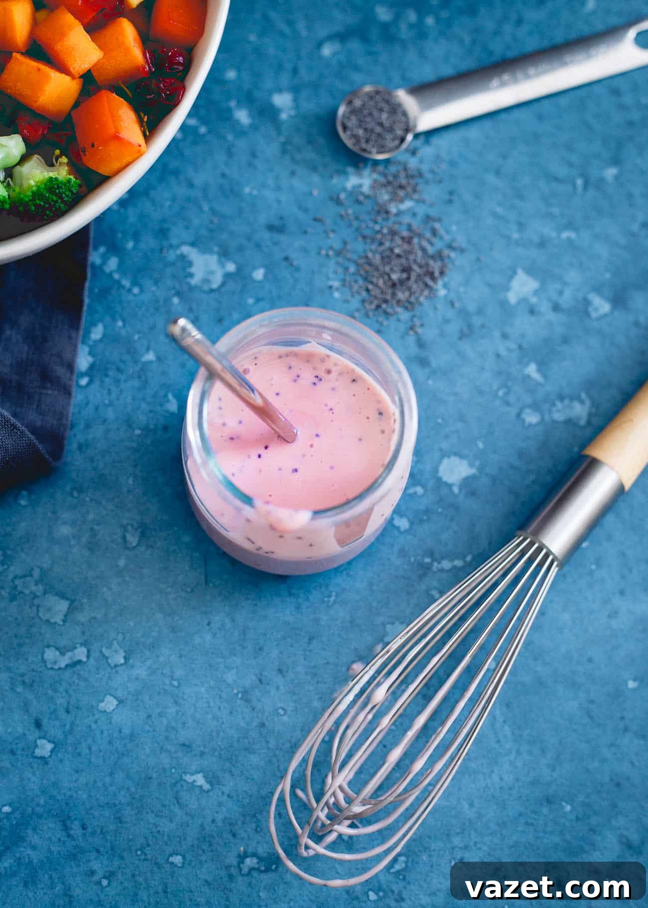 A glass jar filled with homemade cranberry dressing, featuring a light pink hue, with a whisk resting beside it.