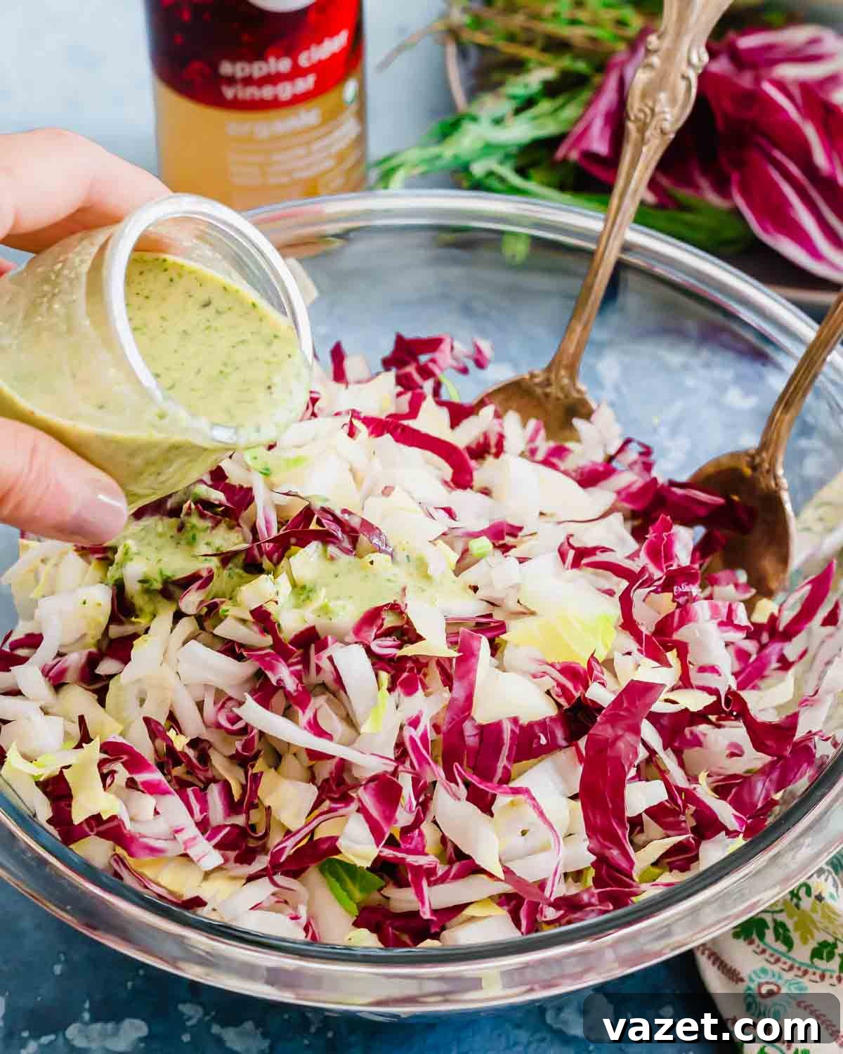 A person drizzling a dressing on an endive radicchio salad.