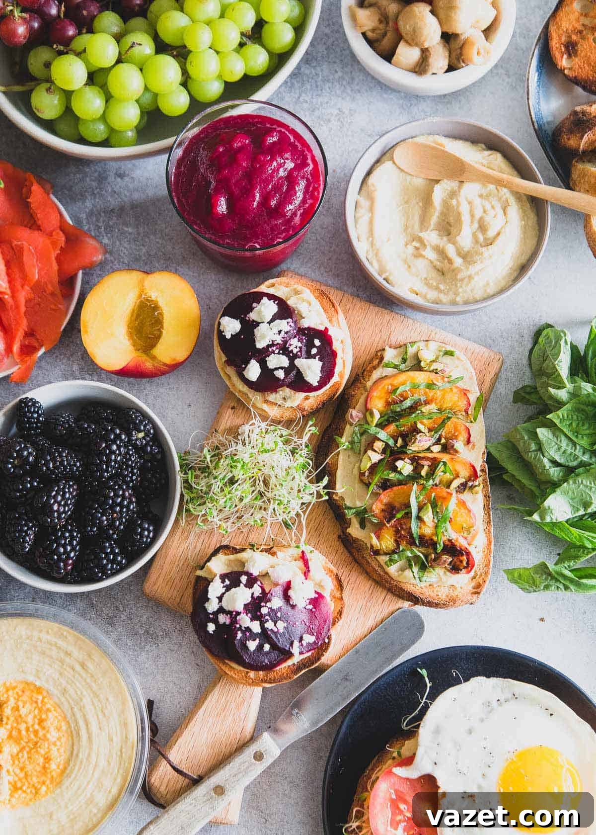 A beautifully arranged healthy hummus toast brunch spread featuring various toppings, perfectly complemented by a glass of simple beet smoothie.