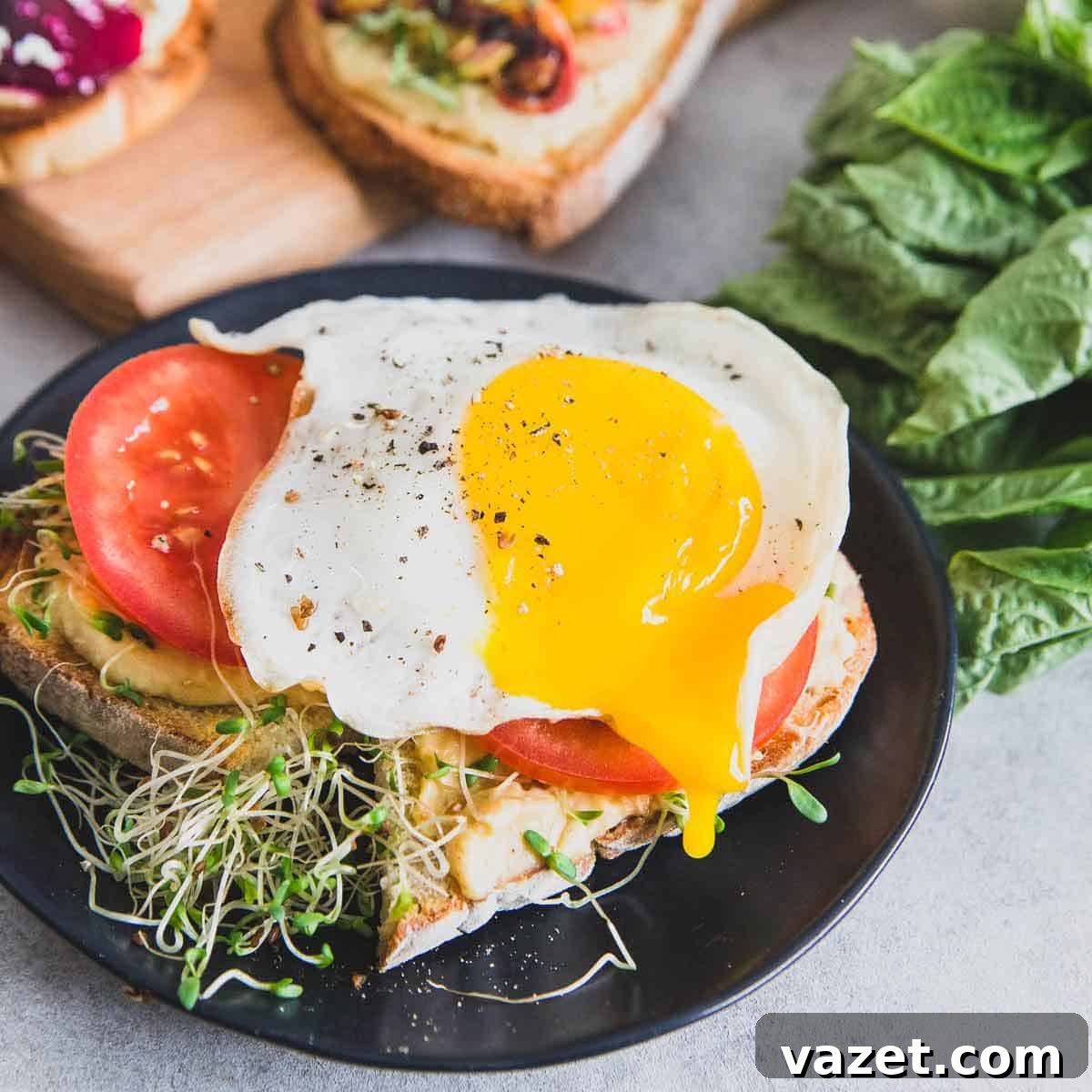 A perfectly runny fried egg crowns sourdough hummus toast with fresh tomato slices, served alongside a delicious and healthy beet smoothie recipe.