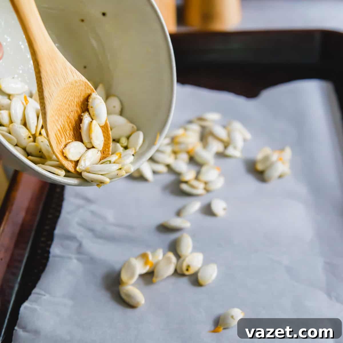 Spreading out seasoned squash seeds onto a parchment lined baking sheet before roasting Spreading out seasoned squash seeds onto a parchment lined baking sheet before roasting