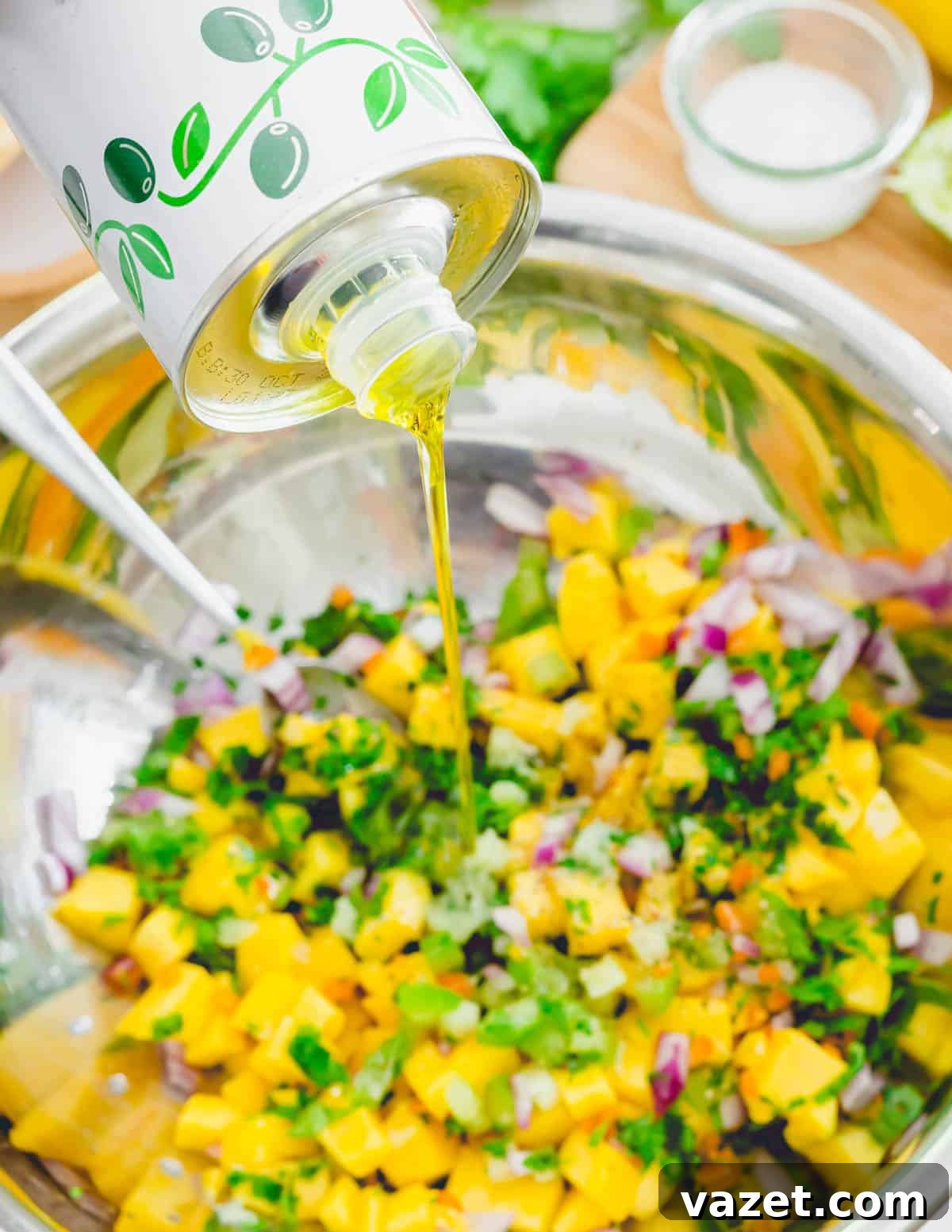 A stream of extra virgin olive oil being poured into a bowl of mango habanero salsa ingredients, preparing for the final mix.