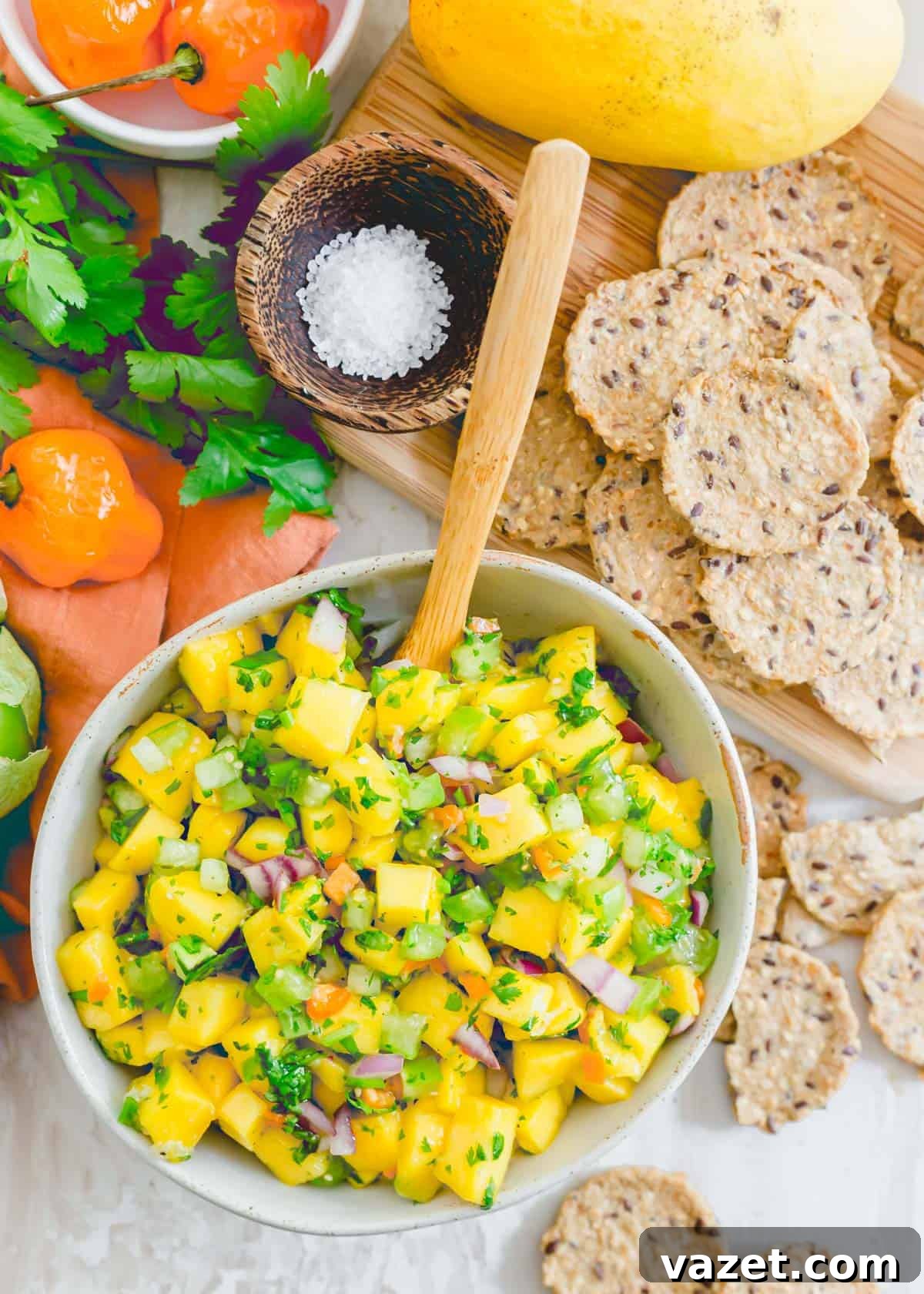 A bowl of fresh mango salsa with habanero peppers, cilantro, red onion, and tomatillos, served with crackers on the side for dipping.