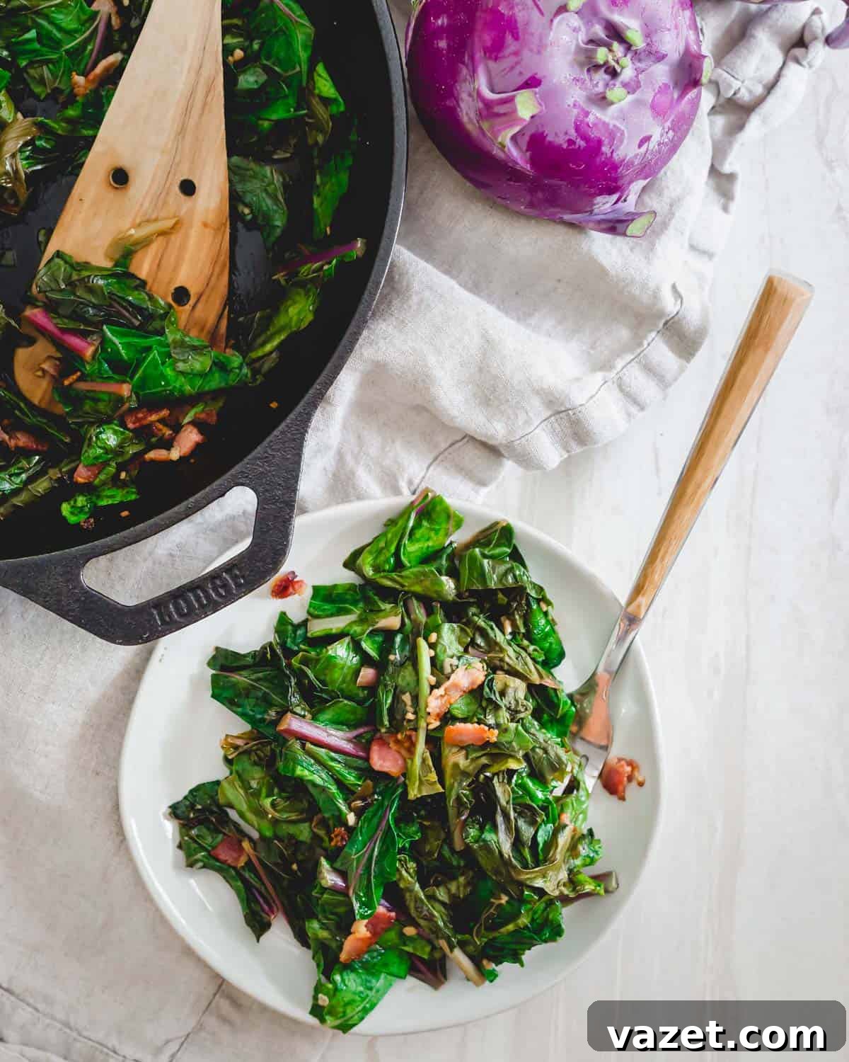 Leafy kohlrabi greens sautéed until tender with garlic, green onions and topped with crispy bacon. Close-up view of leafy kohlrabi greens, sautéed until tender, topped with crispy bacon, fresh garlic, and green onions in a skillet.