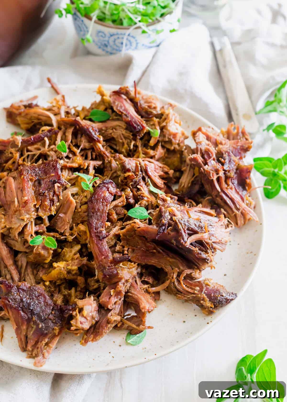 Shredded braised leg of lamb on a plate with fresh oregano can be used in a variety of different lamb dishes. Shredded braised leg of lamb on a plate with fresh oregano can be used in a variety of different lamb dishes.