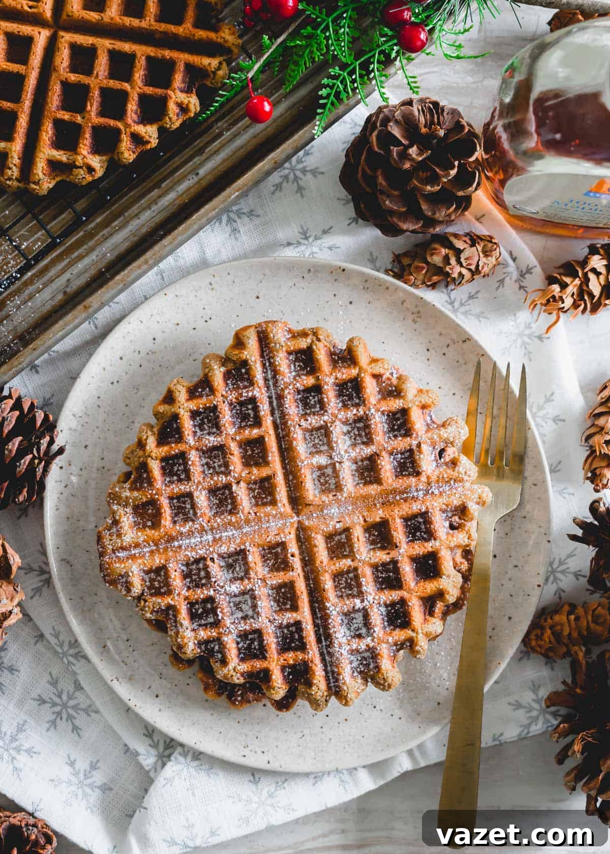 Fluffy gingerbread waffles dusted with powdered sugar and a drizzle of maple syrup, served on a white plate with a fork.