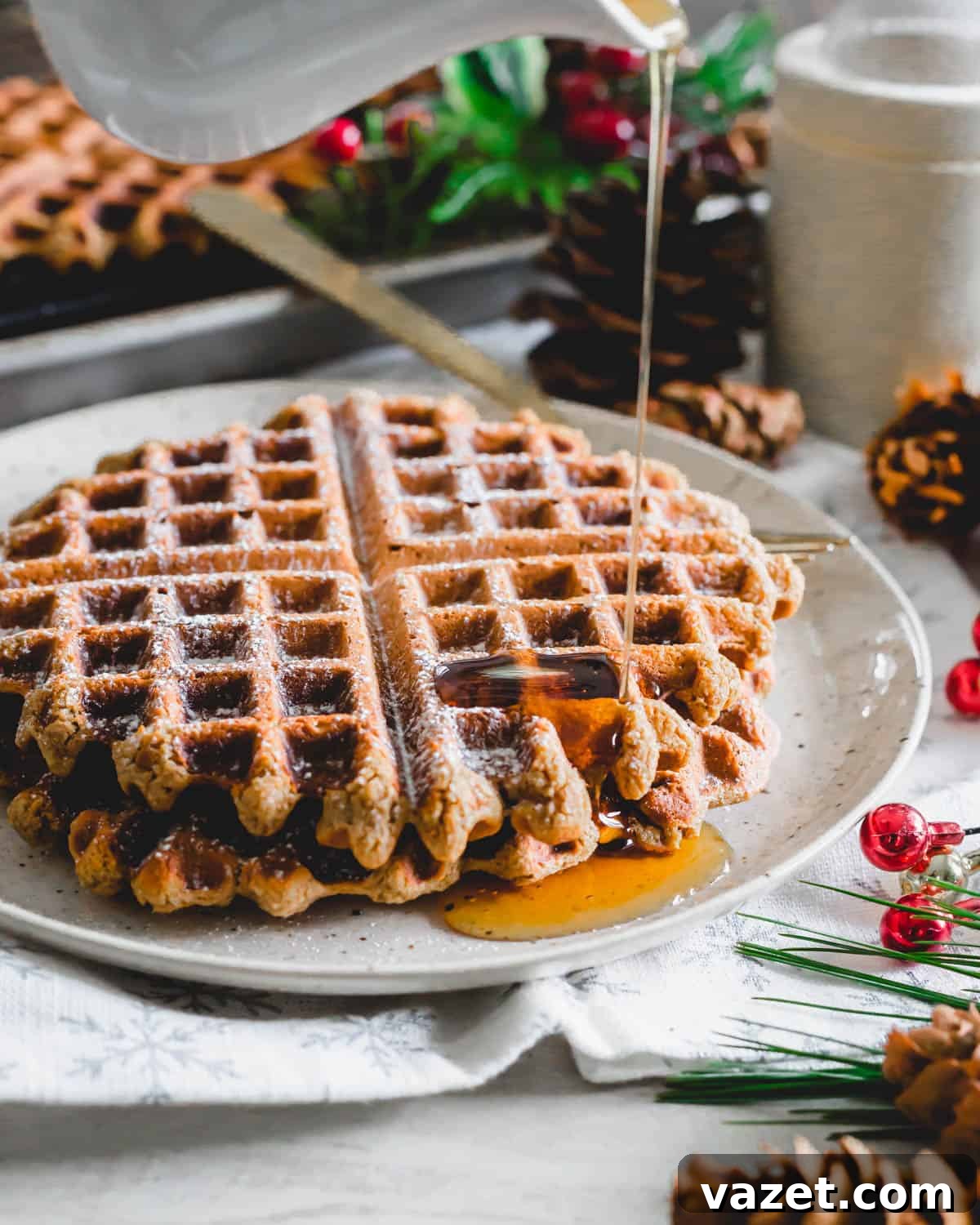 Rich maple syrup being poured generously over a stack of warm gingerbread waffles on a white plate, ready to be served.