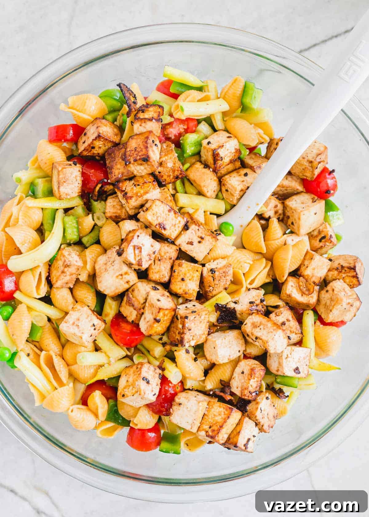 Finishing Touches: Tofu Integrated into Pasta Salad Skillet cooked tofu is gently folded into a vibrant pasta salad in a clear glass bowl, ready to be served.