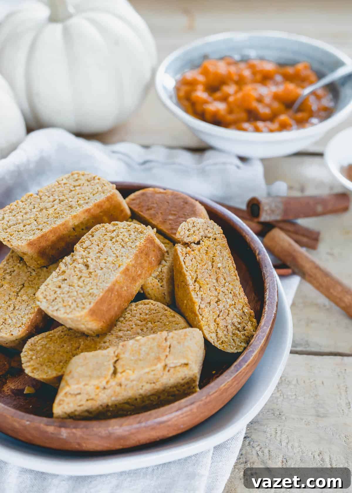 Pumpkin biscotti cookies on a round wooden plate with cinnamon sticks and pumpkin puree in the background.