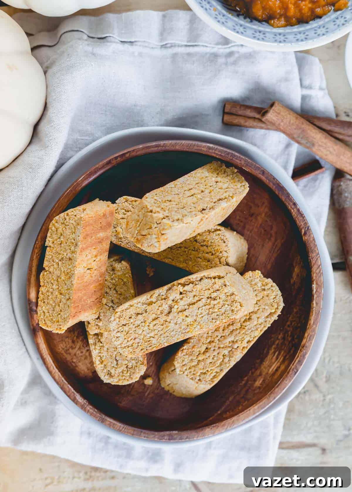 Gluten-free, vegan pumpkin spice biscotti piled on a wooden plate with a neutral cloth napkin beneath it.