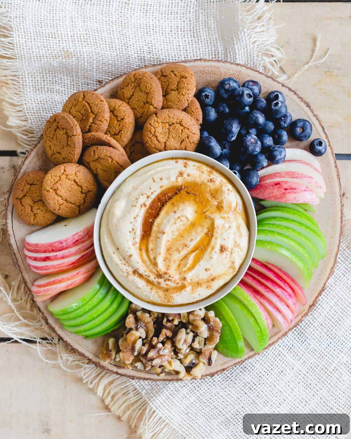Pumpkin ricotta dip with maple syrup and pumpkin pie spice in a serving bowl on a wood board with various dippers surrounding it.