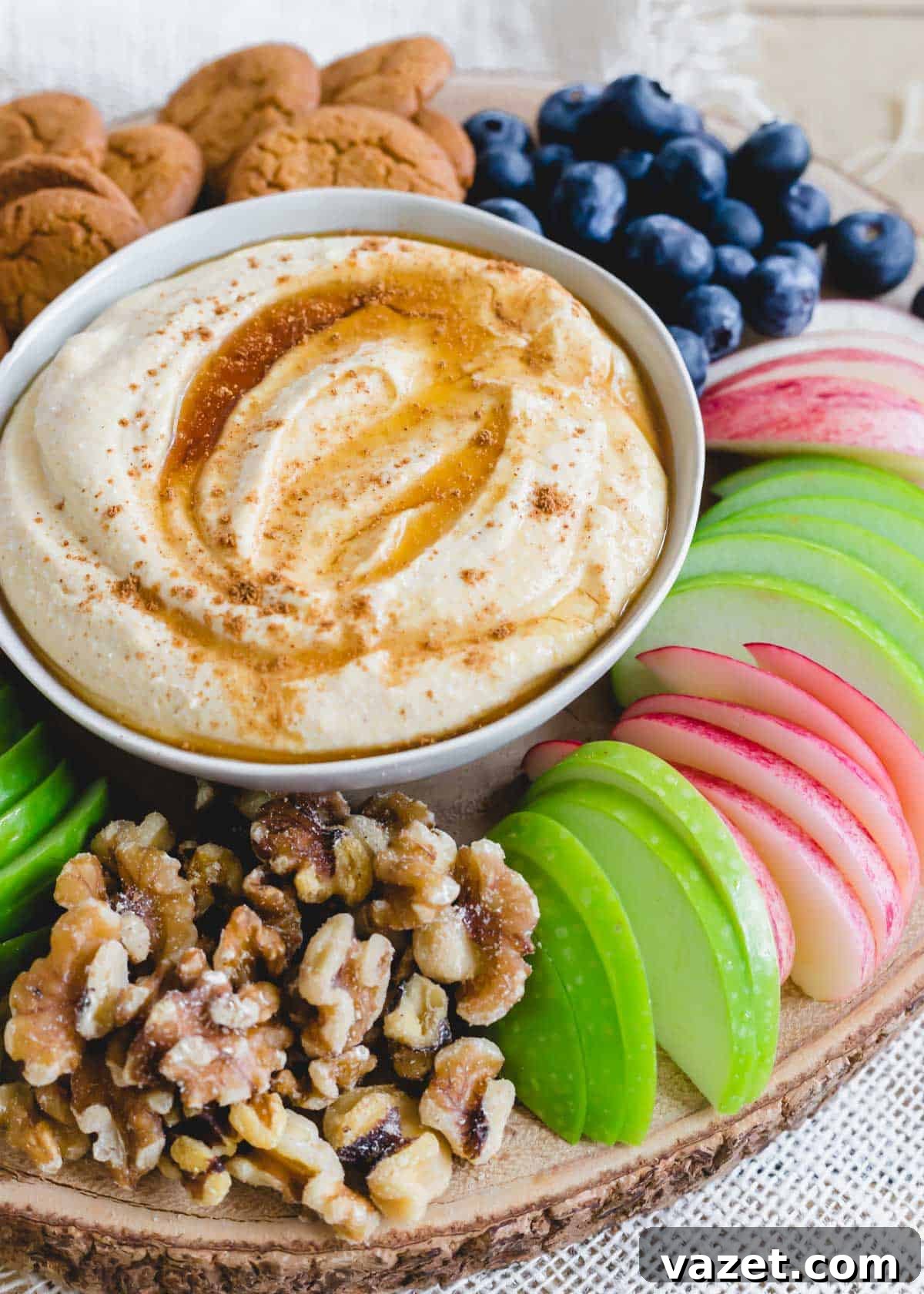 Whipped ricotta dessert dip served in a small bowl with fresh apple slices, walnuts, gingersnaps, and blueberries arranged around it.