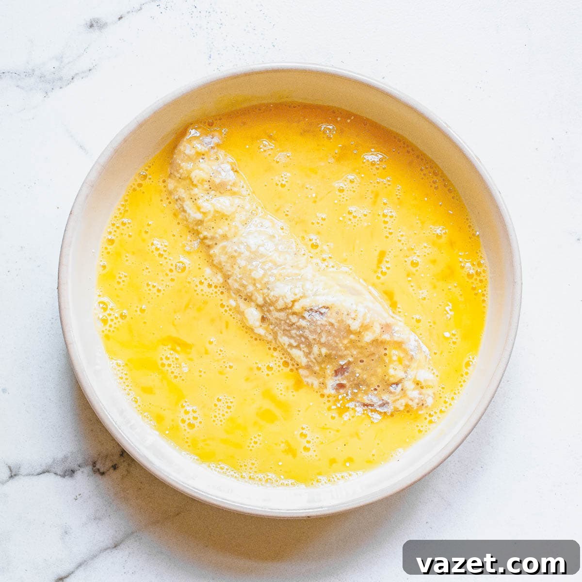 Prepping Chicken Tenders for Air Frying: Egg Wash Coating Chicken tenders being dredged in an egg wash, a crucial step for achieving ultra-crispy air fryer buffalo chicken.
