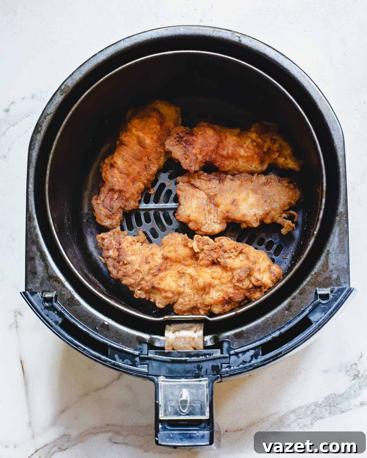 Freshly Air-Fried Buffalo Chicken Tenders in the Basket Crispy chicken tenders coated in buffalo sauce resting in an air fryer basket after cooking.