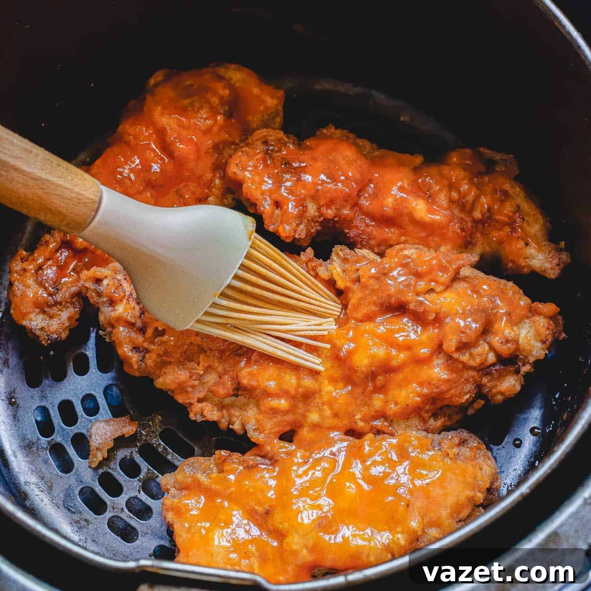 Applying Buffalo Sauce to Freshly Cooked Air Fryer Tenders Brushing vibrant buffalo sauce onto hot, air-fried chicken tenders while they are still in the air fryer basket.