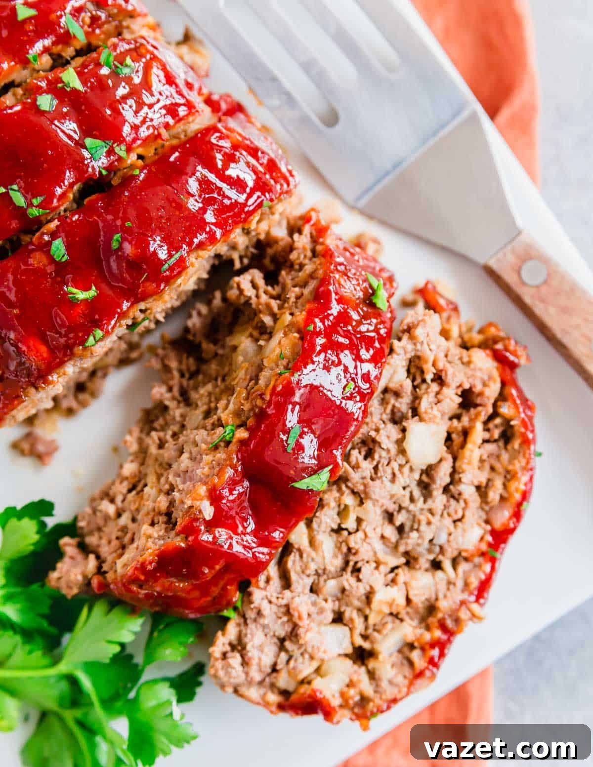 Next-Level Meatloaf 2 Perfectly sliced meatloaf on a white plate, generously coated with a glistening sweet and tangy glaze, garnished with fresh parsley.