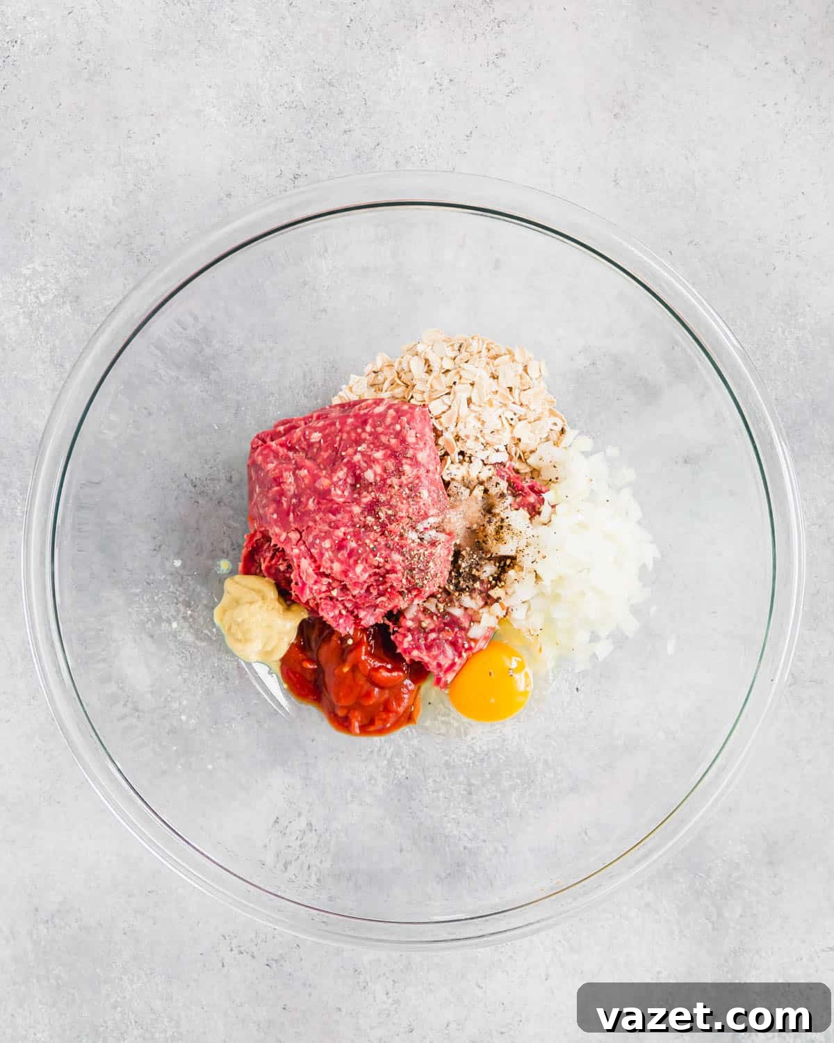 Meatloaf ingredients in a large glass bowl. Fresh meatloaf ingredients, including ground beef, oats, and diced onions, perfectly arranged in a large glass mixing bowl, ready for preparation.