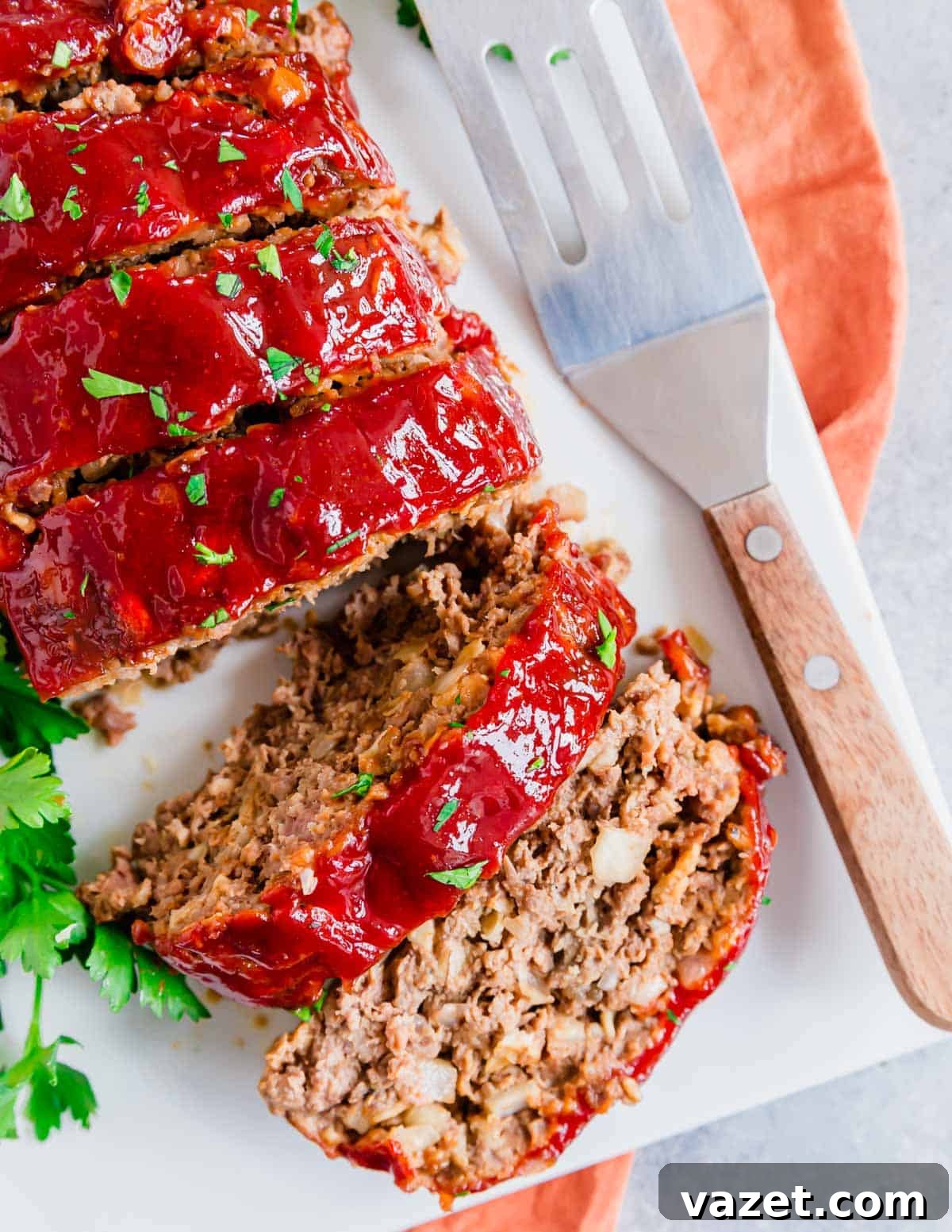 Two slices of glazed meatloaf showing the tender inside on a white plate. Two generous slices of tender, glazed meatloaf, revealing the moist and flavorful interior, served on a pristine white plate.