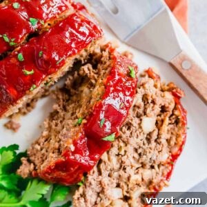 Next-Level Meatloaf 3 Sliced meatloaf on a white plate with a sweet and tangy glaze and fresh parsley.