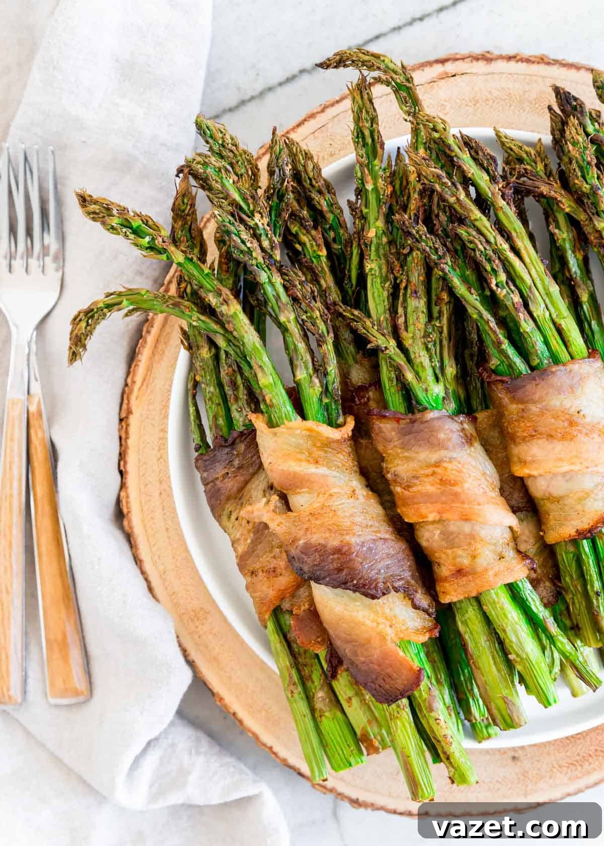 Air Fried Bacon Wrapped Asparagus Perfection 2 Air fried asparagus bunches wrapped in crispy bacon on a plate with forks to the side.