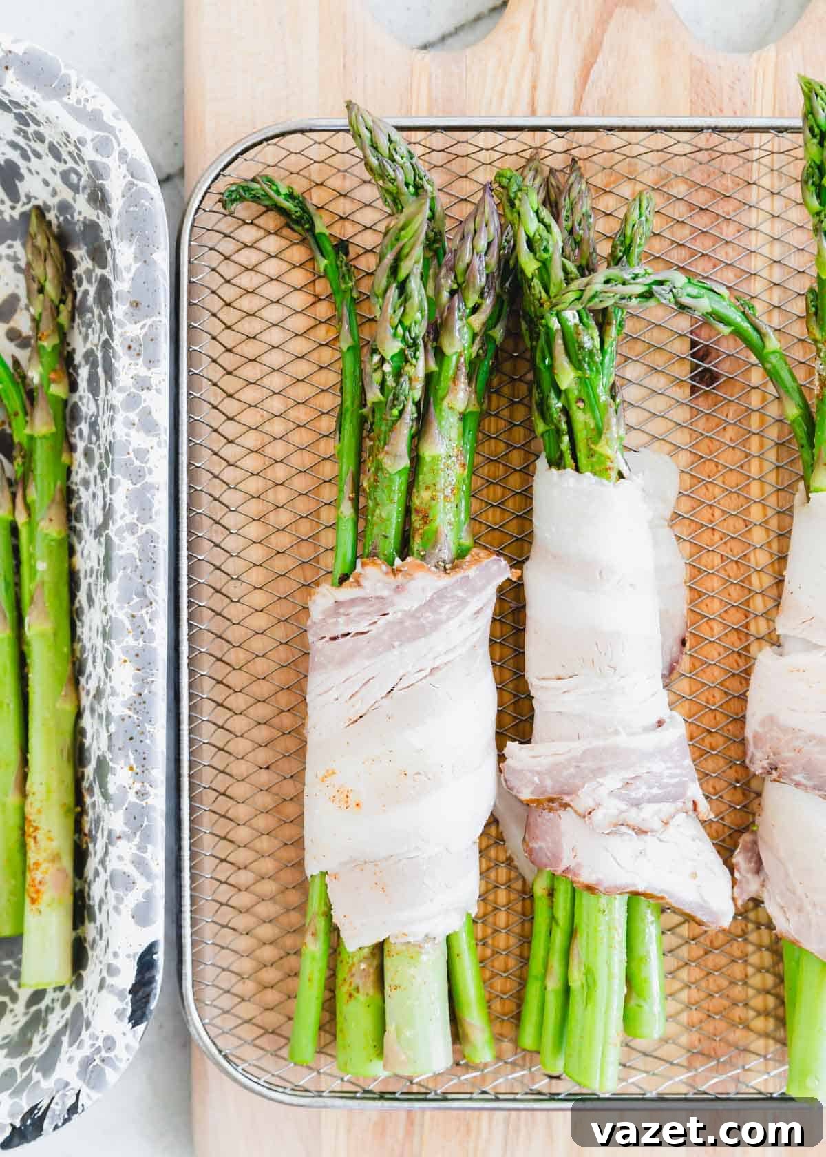 Air Fried Bacon Wrapped Asparagus Perfection 3 Asparagus bundles wrapped in raw bacon on a wire air fryer rack.