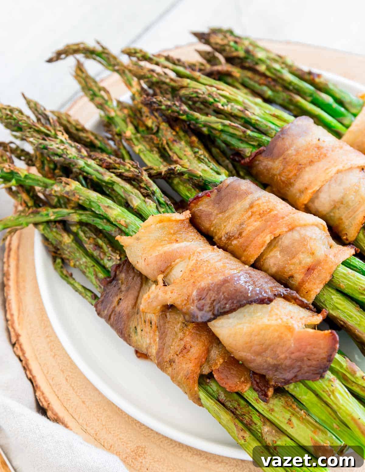 Air Fried Bacon Wrapped Asparagus Perfection 5 Air fryer asparagus wrapped bacon bundles stacked on a white plate.