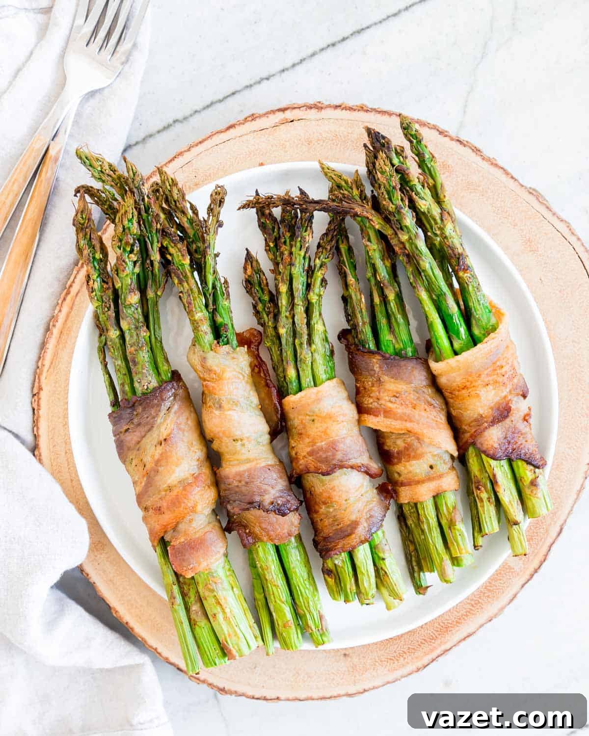 Air Fried Bacon Wrapped Asparagus Perfection 6 Bacon wrapped asparagus on a white plate.