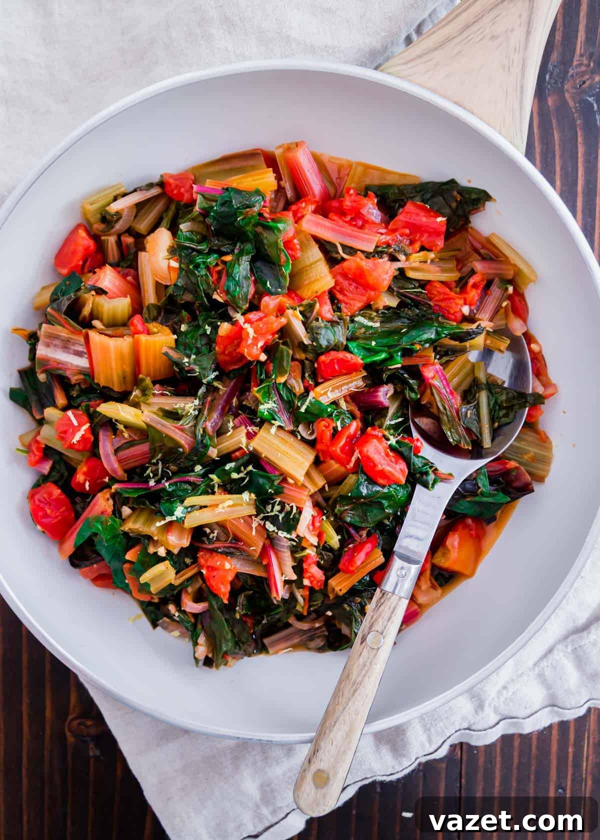 Quick Sauteed Swiss Chard 2 A vibrant close-up of freshly cooked sautéed Swiss chard with garlic, onions, and diced tomatoes, ready to be served. A lemon wedge rests on the side.