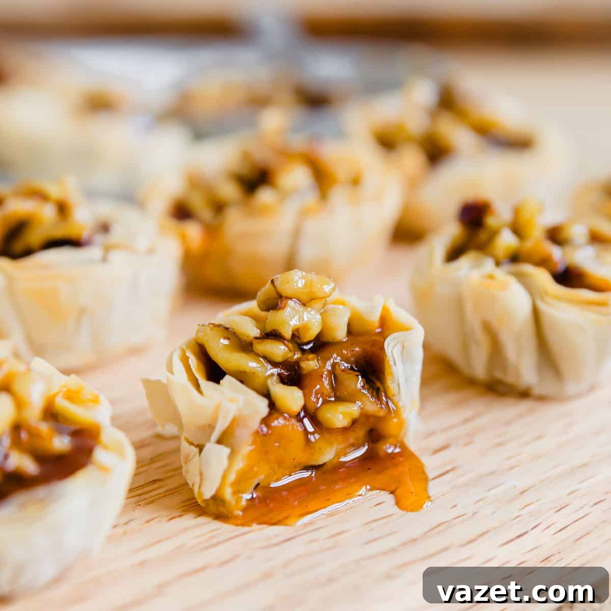 Bite-Sized Pumpkin Delights 7 A pumpkin pie bite, artfully cut in half, showcasing its custardy filling and flaky crust, with walnuts and maple syrup topping nearby on a cutting board.