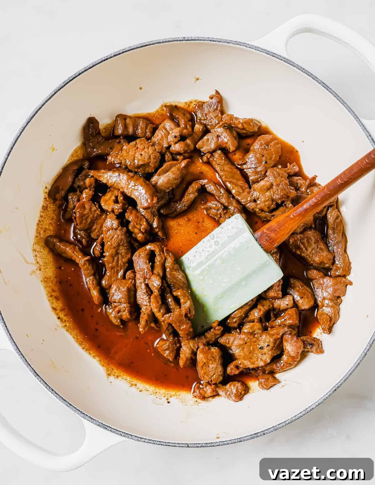 A close-up shot of browned, flavorful beef strips cooking in a pan with a spatula, indicating perfect searing.