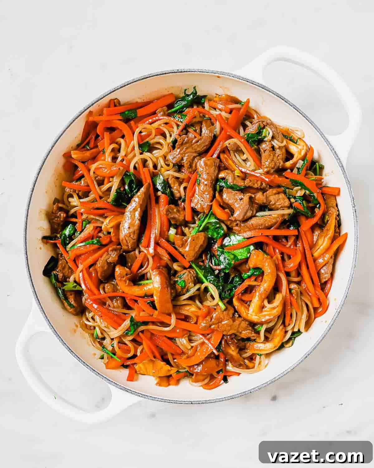 A close-up view of a large pan filled with freshly cooked sweet potato glass noodles, tender beef, and a vibrant assortment of stir-fried vegetables, ready to be combined.