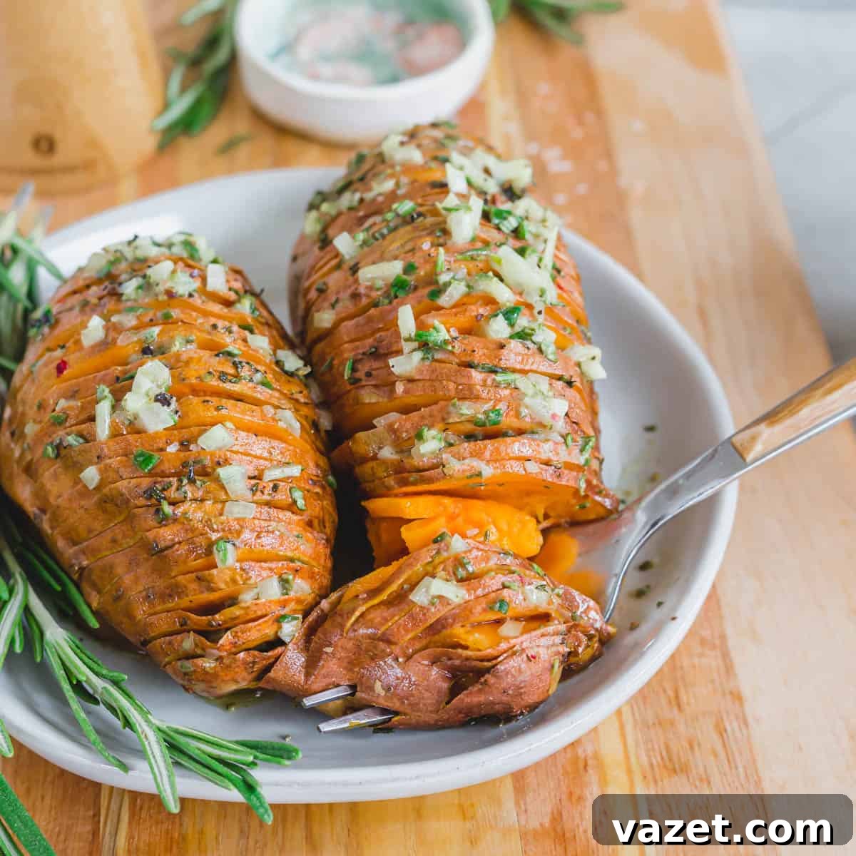 A forkful of roasted hasselback sweet potatoes on a plate with fresh rosemary sprigs. A forkful of roasted hasselback sweet potatoes on a plate with fresh rosemary sprigs.