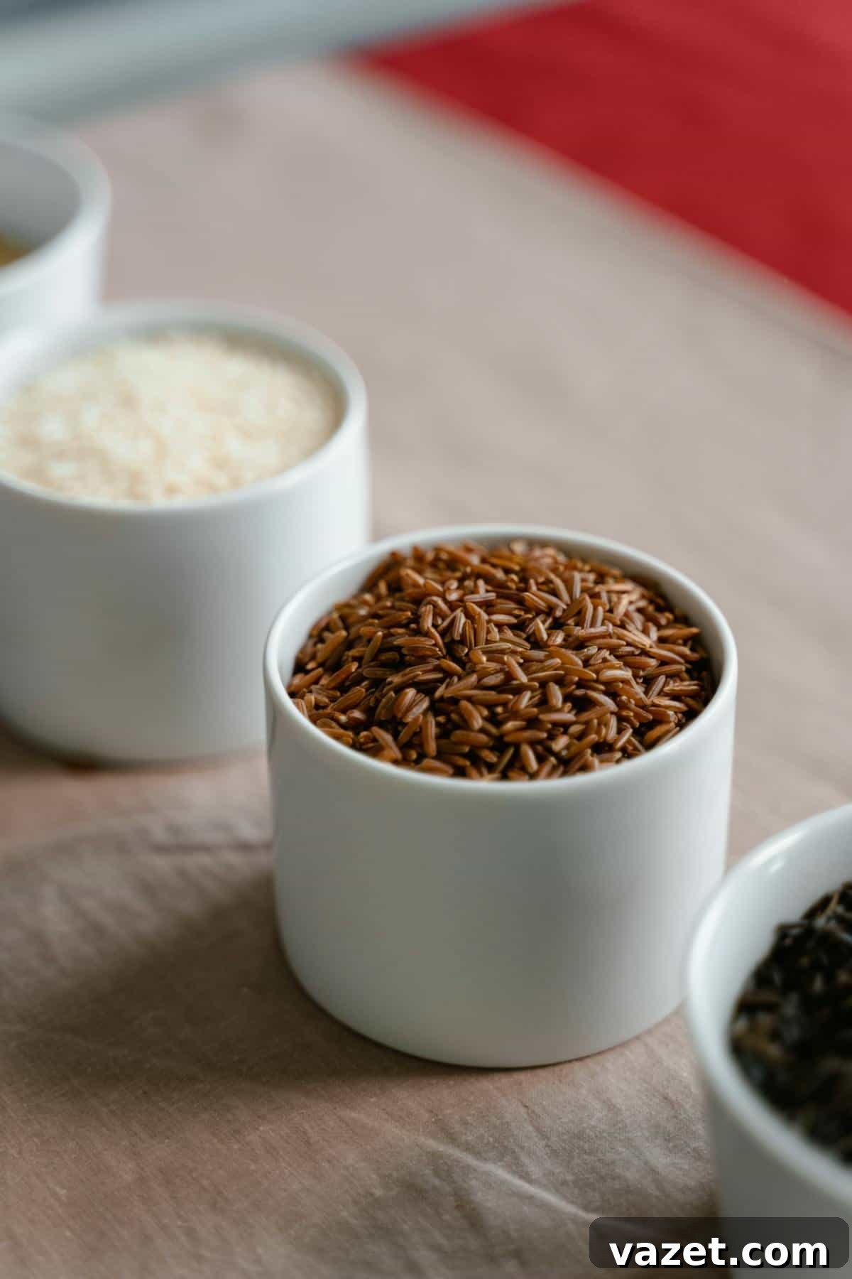 A Rice Odyssey Discovering Grains Beyond Basmati 3 A close-up of a white bowl filled with brown rice on a table, with other bowls of various types of rice blurred in the background.