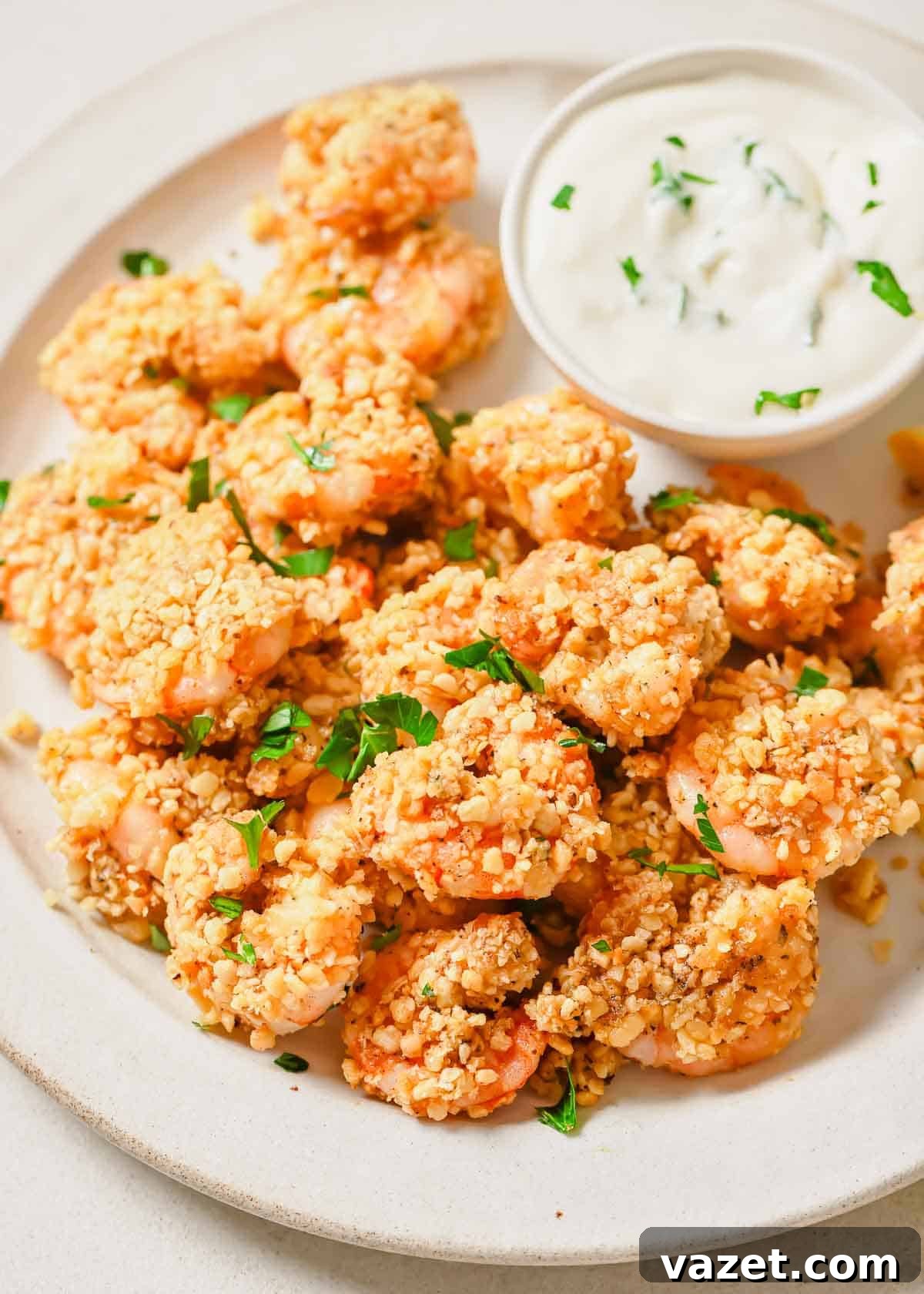 Quick Baked Shrimp Poppers 2 A plate of golden-brown baked popcorn shrimp, garnished with fresh parsley and lemon wedges, alongside a small bowl of creamy dipping sauce.