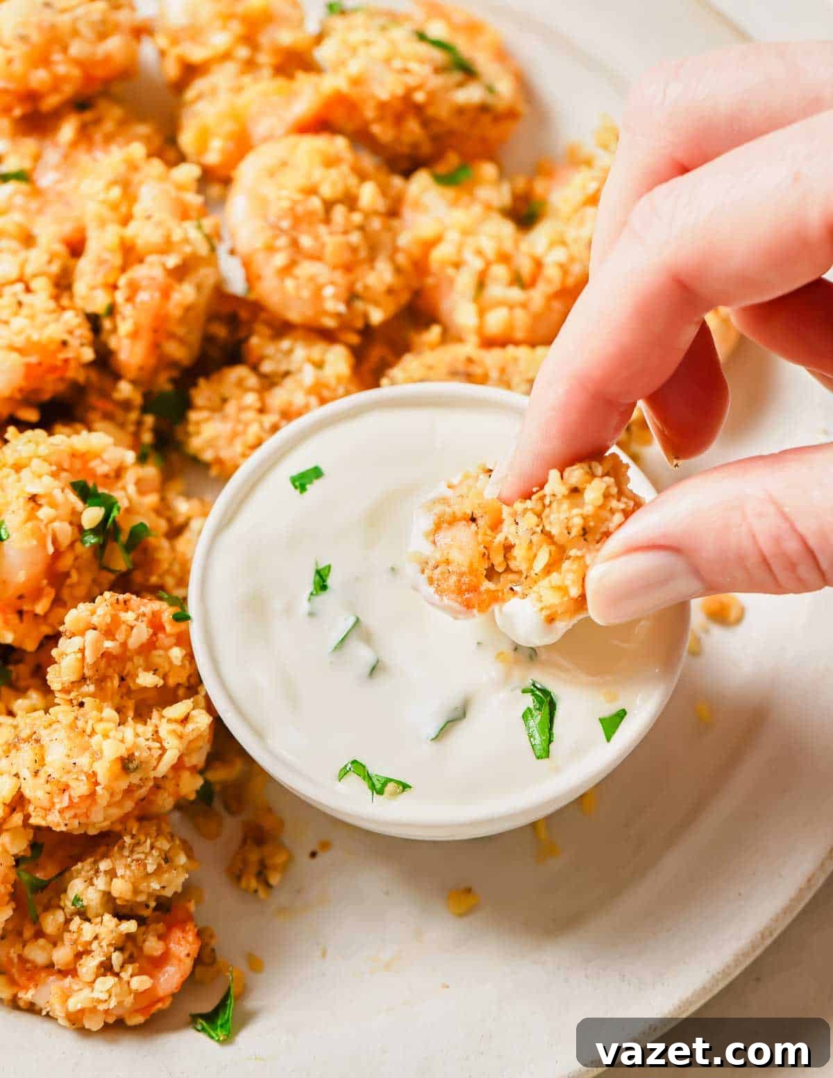 Quick Baked Shrimp Poppers 9 A person's hand dipping a crispy baked popcorn shrimp into a bowl of creamy white sauce, highlighting its golden texture.