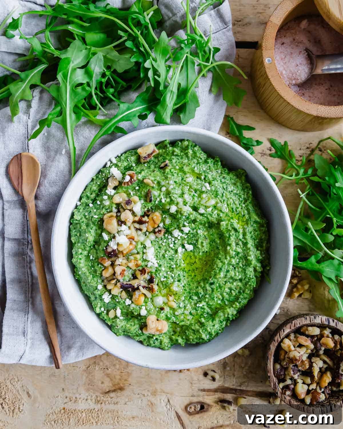 A bowl of arugula pesto with walnuts and crumbled parmesan.