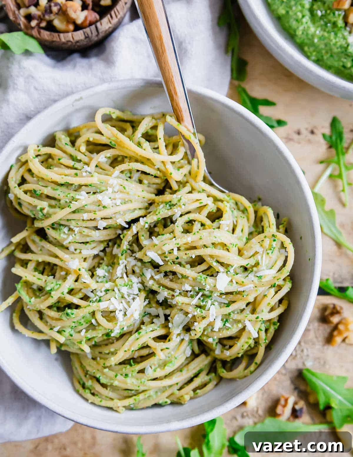 A bowl of spaghetti tossed with arugula pesto wrapped around a fork.