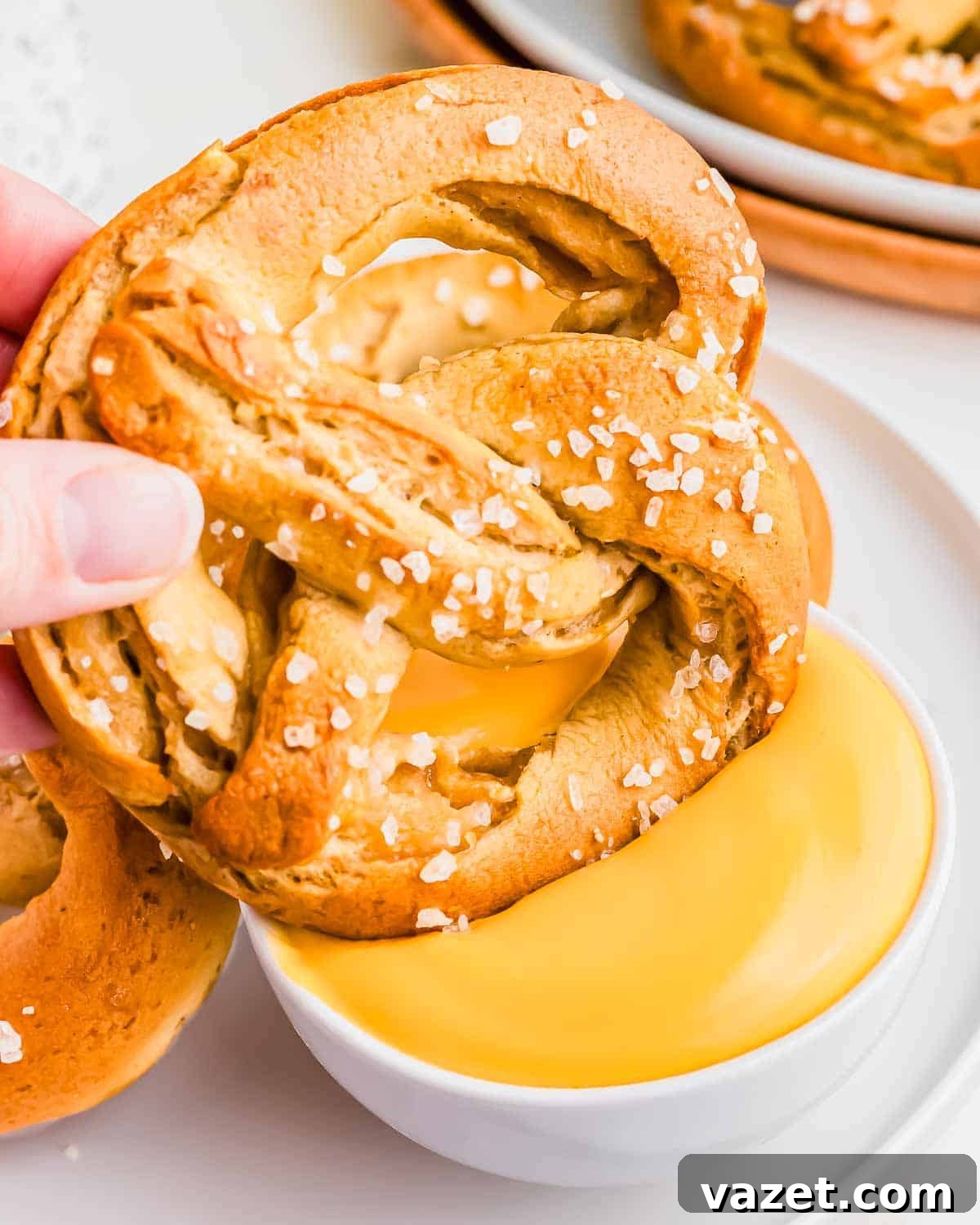 Cloud-Soft Gluten-Free Pretzels 12 A hand holding a pretzel over a bowl of cheese sauce.