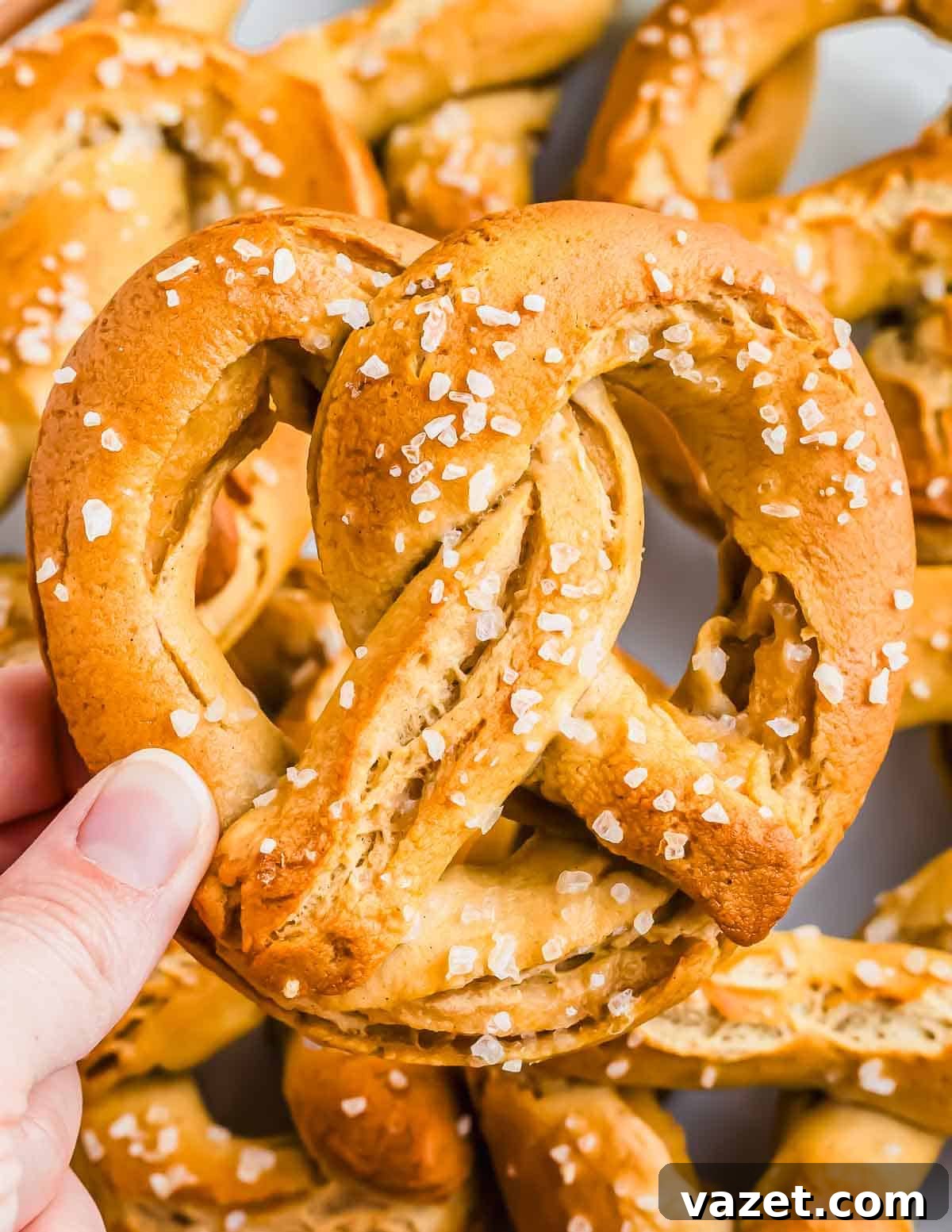 Cloud-Soft Gluten-Free Pretzels 13 A hand holding a salted gluten free pretzel with several other pretzels in the background.