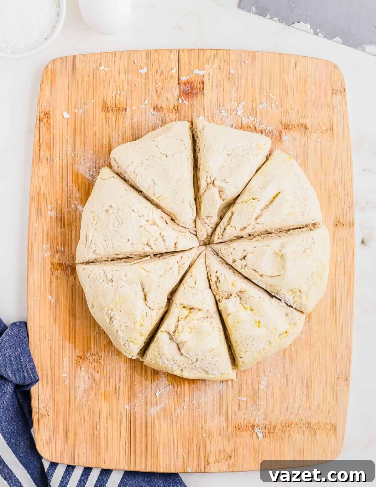 Cloud-Soft Gluten-Free Pretzels 7 A round piece of dough cut into eight triangular sections on a wooden cutting board, with a blue and white striped cloth partially visible in the lower left corner.
