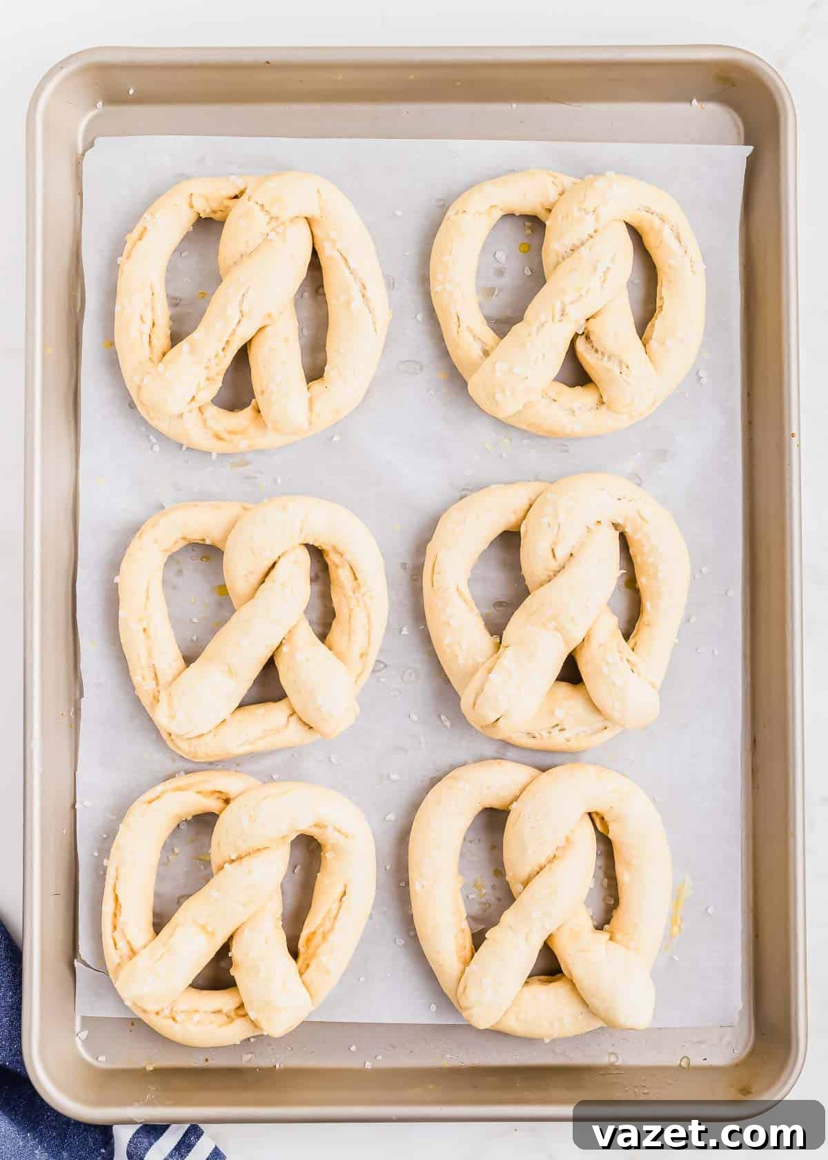 Cloud-Soft Gluten-Free Pretzels 10 A baking tray with six unbaked gluten-free pretzels arranged in two rows of three, lined with parchment paper, ready to be baked.