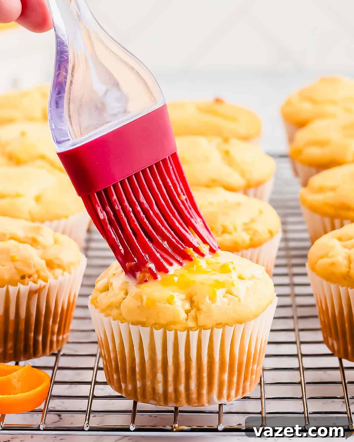 Zesty Orange Muffins 8 A hand expertly brushing orange glaze onto warm muffins on a cooling rack, creating a delicious shine.