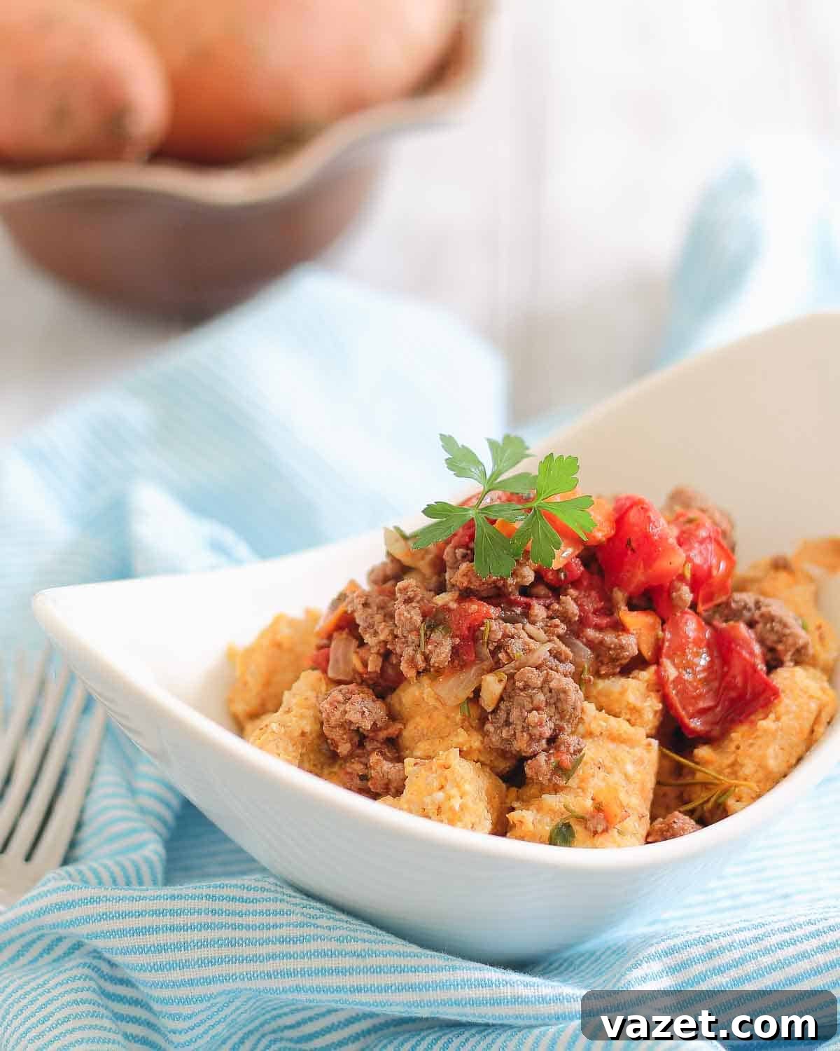 A white bowl filled with sweet potato gnocchi topped with cooked ground meat and cherry tomatoes, garnished with parsley.