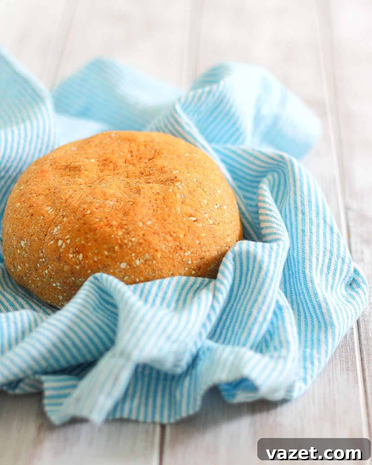 A round shaped dough for making gnocchi on a blue and white striped cloth on a wooden surface.