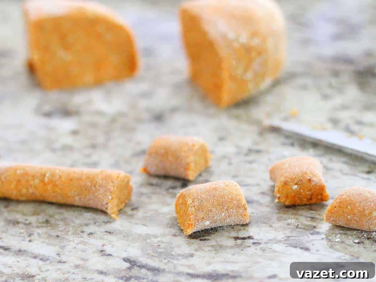 Close-up of raw gnocchi dough pieces being cut on a marble countertop, with some rolled dough and a knife visible in the background.