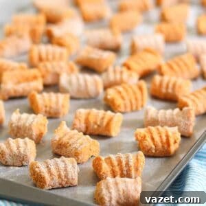 A baking tray filled with uncooked homemade sweet potato gnocchi, lightly dusted with flour. The gnocchi pieces are evenly spaced and have a ridged texture. The tray is on a striped blue cloth.