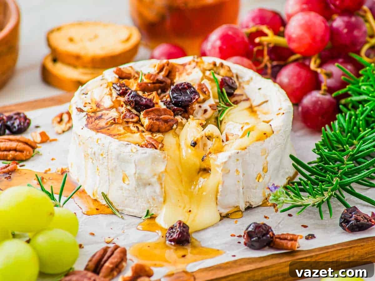 Honey-Kissed Baked Brie 8 A wheel of baked brie cheese with honey is topped with pecans, dried cranberries and fresh rosemary, with cheese melting out. Fresh grapes, crackers, and rosemary sprigs are arranged nearby.