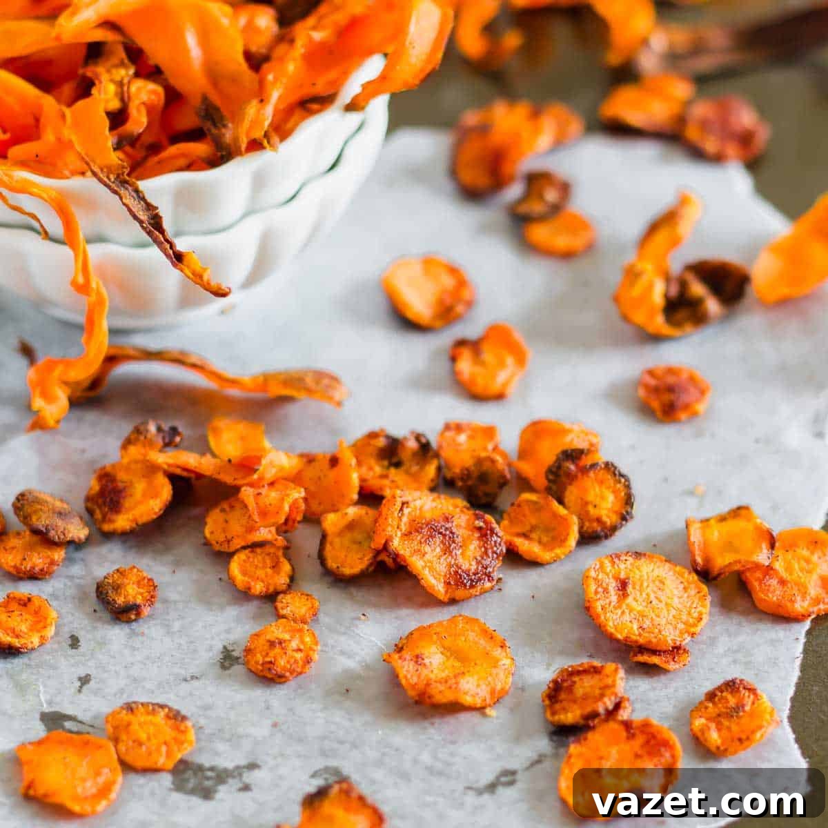 Crunchy Roasted Carrot Crisps 2 A bowl of crispy carrot chips next to scattered chips on parchment paper, highlighting their golden-orange color and crunchy texture.
