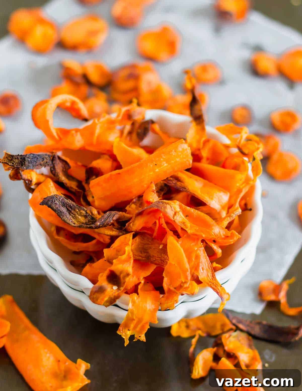 Crunchy Roasted Carrot Crisps 3 A bowl of homemade carrot chips on a gray surface, showcasing crispy, orange slices with slightly charred edges, ready to be enjoyed.