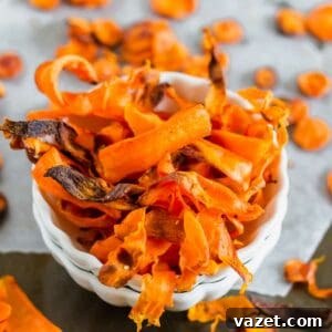 A bowl of homemade carrot chips on a gray surface, showcasing crispy, orange slices with slightly charred edges.